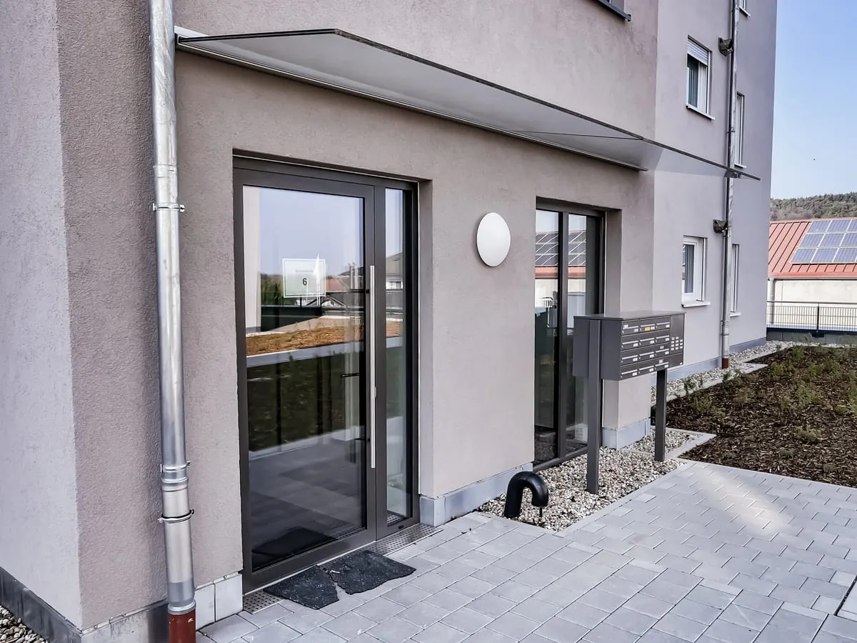 Glasvordach mit Wandmontage am Eingang eines Mehrfamilienhauses, weitere Ansicht