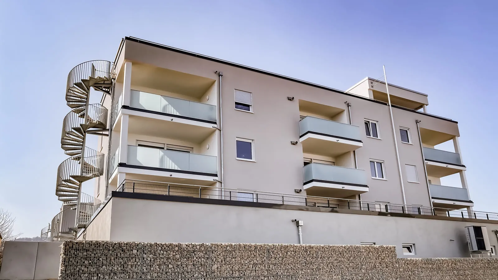 Verzinkte Spindeltreppe an einem Mehrfamilienhaus mit Balkongeländer aus Glas