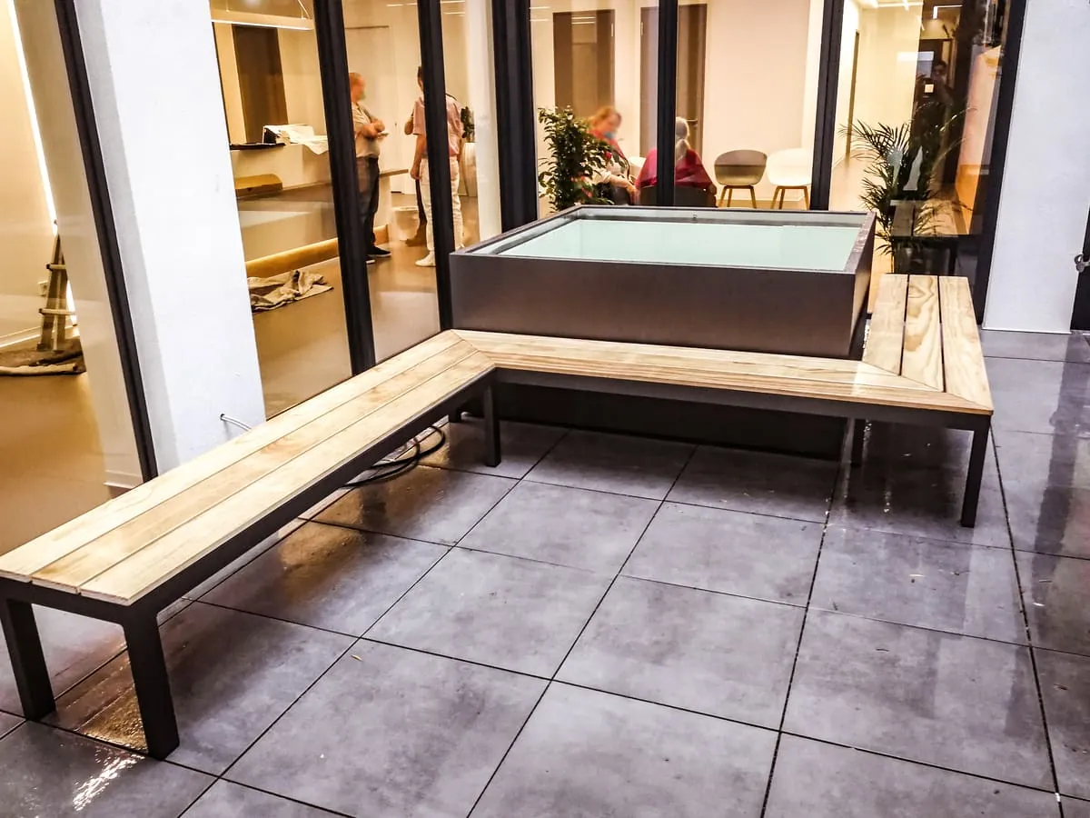 Sitzbank aus Stahl und Holz mit Pflanzgefäß im Innenhof